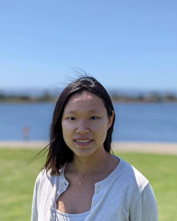 image of East Asian woman outside with a blurry background of green grass and blue water