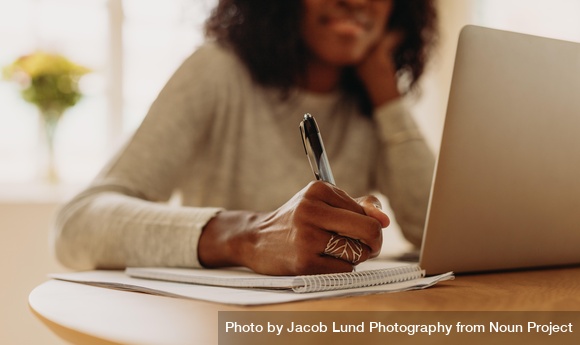 Businesswoman Taking Notes Sitting At Desk At Home